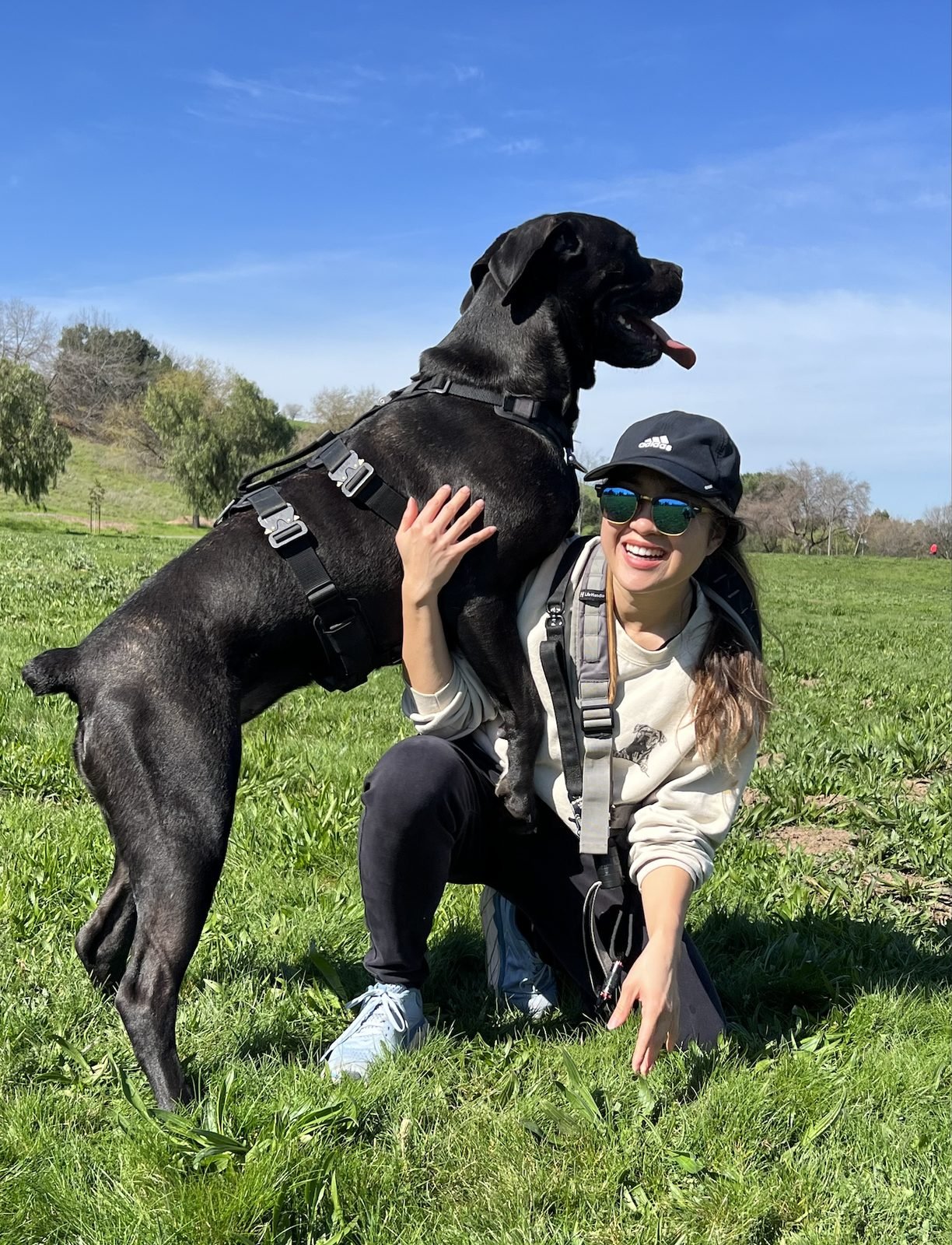 Jasmine smiling in a sunny grass field with Nova, their Cane Corso, leaning against her shoulder